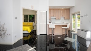 Une cuisine moderne avec un tabouret de bar, un coin repas avec une chaise jaune et une chambre à coucher avec une couvre-lit jaune.