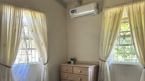 Une chambre à coucher comprenant un lit, une commode, un appareil de climatisation et une fenêtre avec des rideaux.