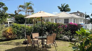 Une terrasse avec une table et des chaises, entourée d’une végétation luxuriante et de plantes en fleurs.
