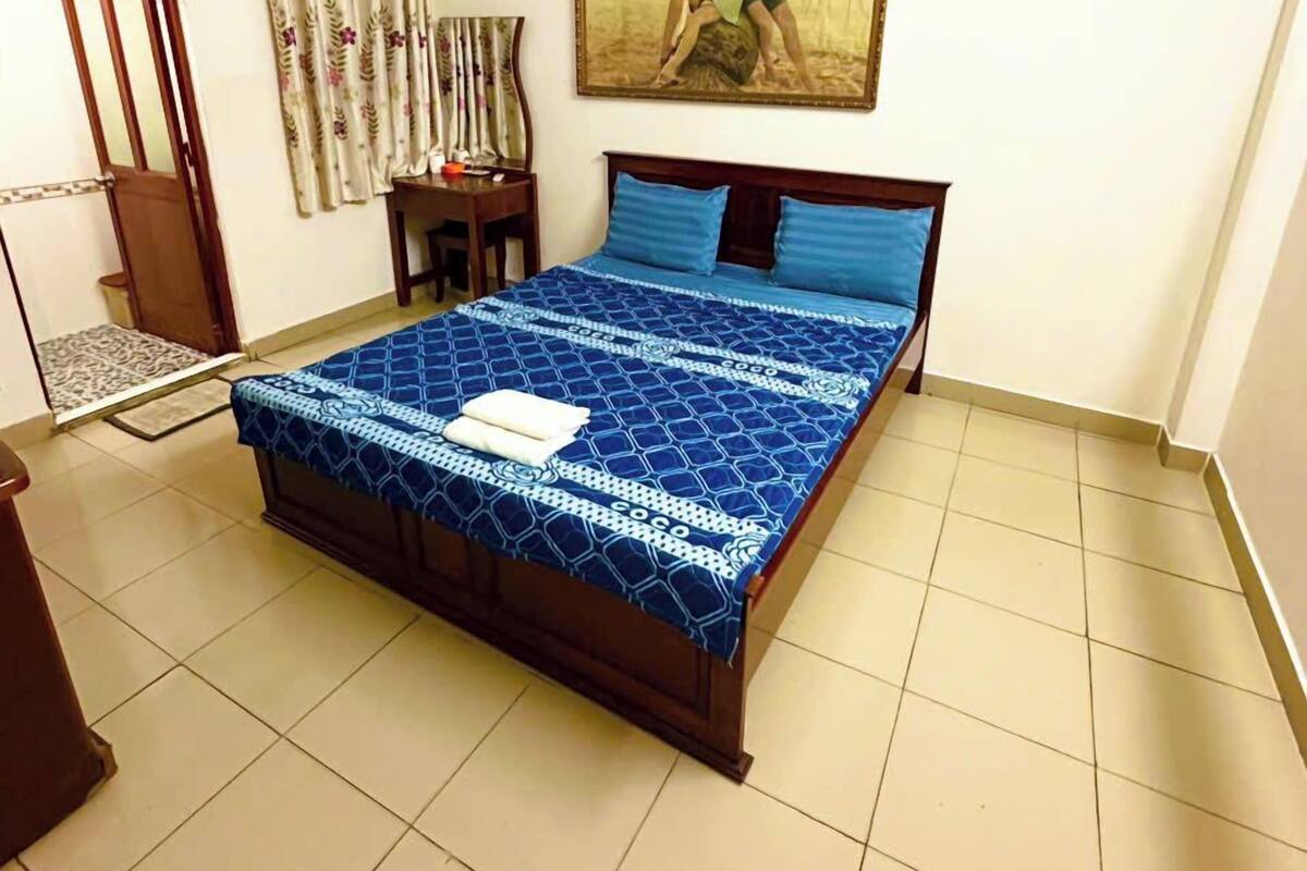 Een slaapkamer met een bed, een deur, een wandairconditioner, een klein tafeltje en een schilderij.