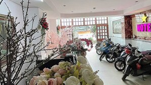 Un hall d’hôtel avec un comptoir d’accueil, des compositions florales, des luminaires au plafond et des motos garées.