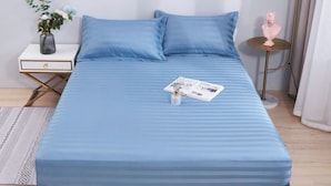 Un lit bien fait, avec un matelas et des oreillers bleus, une petite table de chevet ornée d’un vase de fleurs et une lampe sur pied.