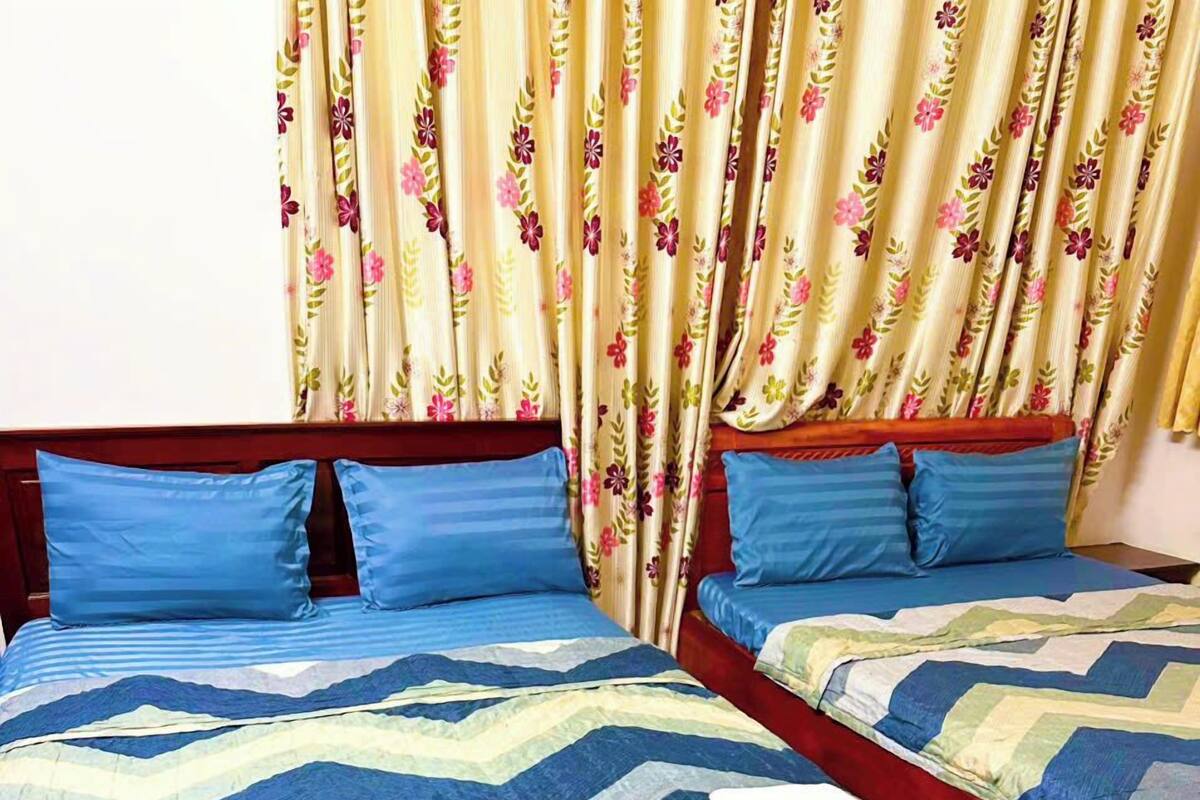 Een kamer met twee bedden, elk voorzien van blauw beddengoed en kussens, en bloemen gordijnen.