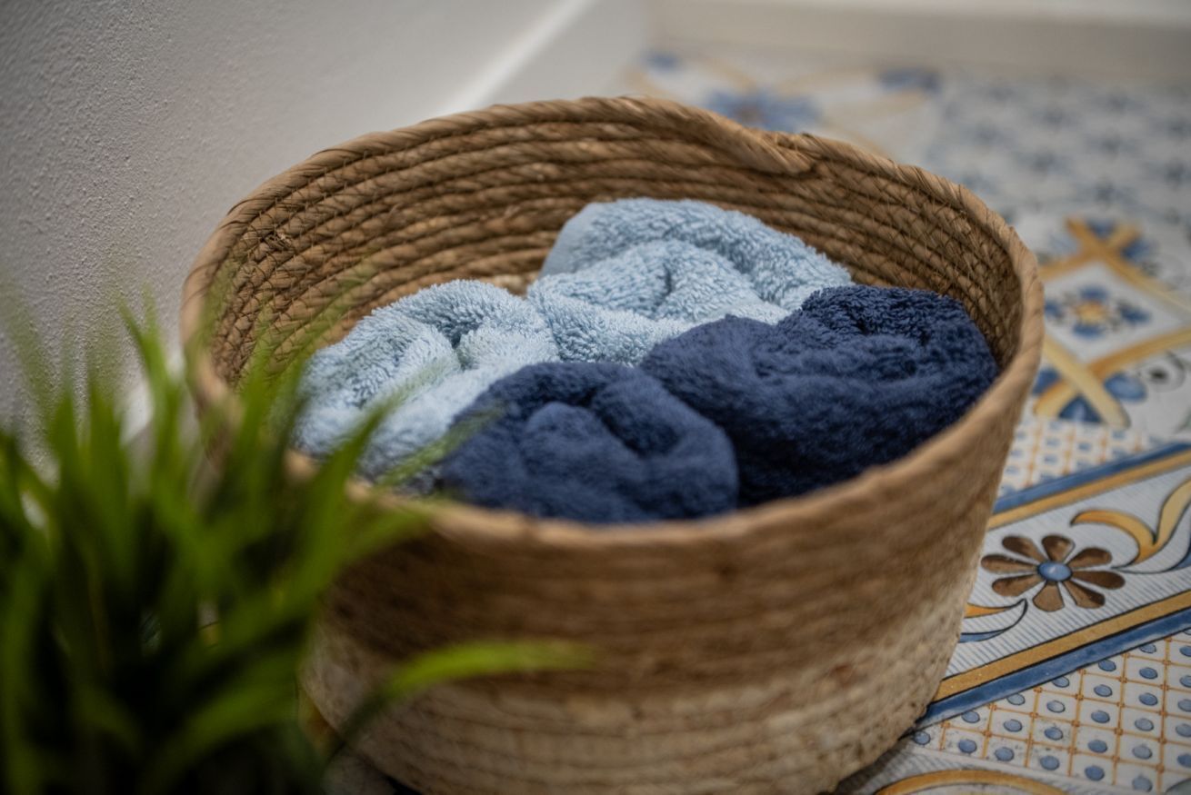 Un panier en osier rempli de serviettes, posé sur un sol à motifs.