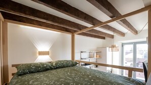 Quarto com cama grande, vigas de madeira, mesa de cabeceira e janela com vista para edifícios.