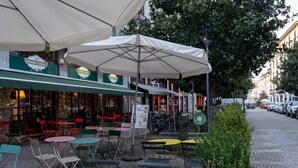 An outdoor café with tables and chairs under umbrellas, a sign for "Panini Turro," and parked bicycles.