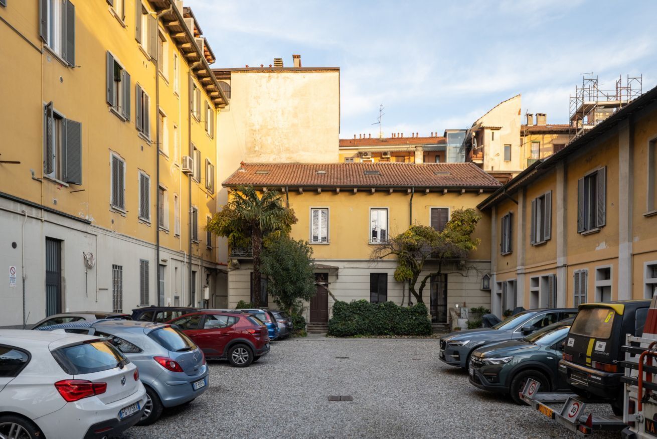 A courtyard with parked cars and buildings with yellow facades and red-tiled roofs.