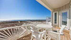 Ein Balkon mit Blick auf den Strand, weiße Stühle und ein Tisch.