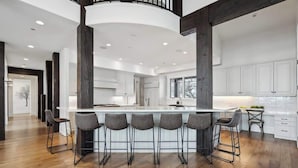 A modern kitchen with a central island, bar stools, and a staircase leading to an upper level.