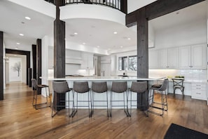A modern kitchen with a central island, bar stools, and a staircase leading to an upper level.