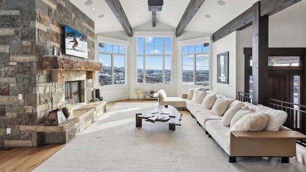 A spacious living room with a stone fireplace, large windows, a white sofa, and a coffee table.