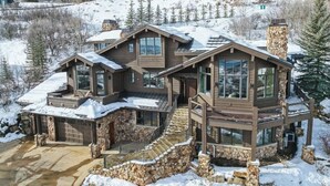 A large, multi-story wooden house with stone accents, a stone staircase, and a snow-covered landscape.