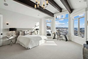 Une chambre avec un grand lit, un bureau et une vue sur un paysage enneigé, visible à travers de grandes fenêtres.