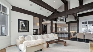 A spacious living room with a large white sectional sofa, a wooden coffee table, and exposed wooden beams on the ceiling.