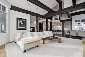 A spacious living room with a large white sectional sofa, a wooden coffee table, and exposed wooden beams on the ceiling.