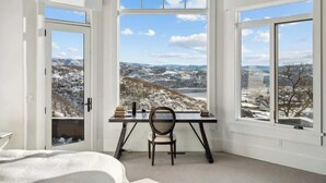 A room with a desk, chair, and large windows with a snowy landscape view.