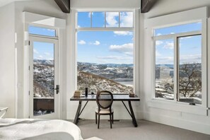 A room with a desk, chair, and large windows with a snowy landscape view.