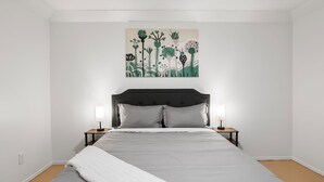 Une chambre à coucher comprenant un lit, deux tables de chevet, une commode et une œuvre d’art accrochée au mur.