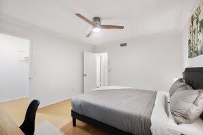 A bedroom with a bed, a ceiling fan, a door, and a wall with a painting. - SOCO Park Creek View  Free (Austin)