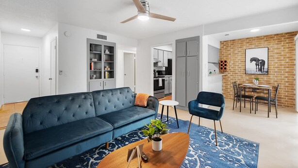 Un salon moderne avec un canapé bleu, une table basse et un coin repas agrémenté d’un mur en briques et d’un tableau encadré.