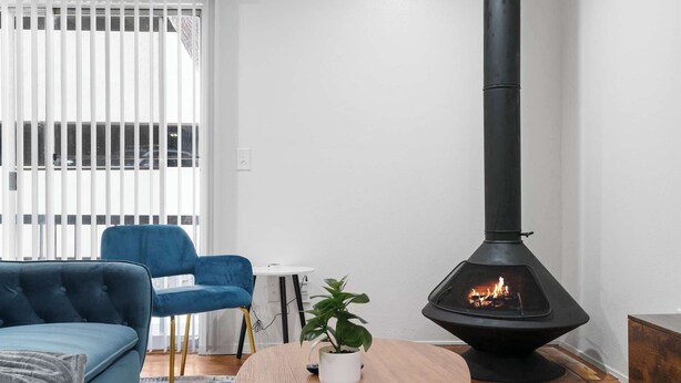 Una sala de estar con un estufa de leña negra, un sofá azul, una mesita blanca y una planta en maceta.