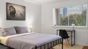 Un dormitorio con cama, escritorio, silla, ventilador de techo y ventana con persianas.