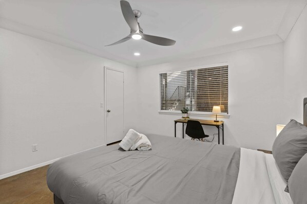 A bedroom with a bed, a desk, a chair, a ceiling fan, and a window with blinds. - SOCO ZEN APT | The Perfect Location | Free Pkg (Austin)