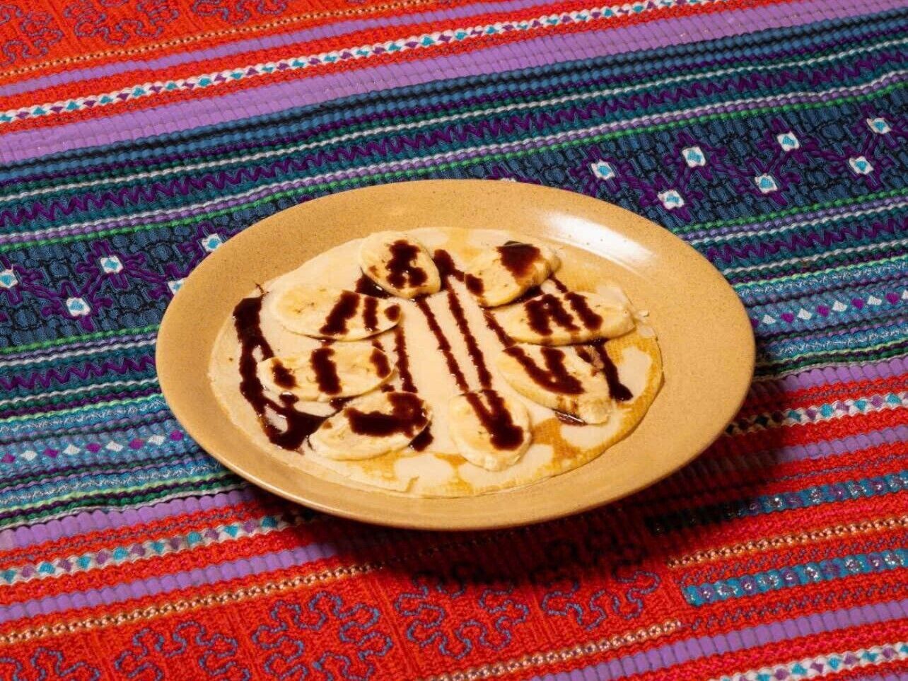 A plate of pancakes with chocolate sauce on a colorful woven tablecloth.