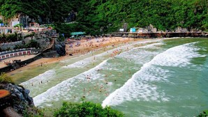 Una playa con varias áreas delimitadas para nadar, costa rocosa y una colina boscosa al fondo.