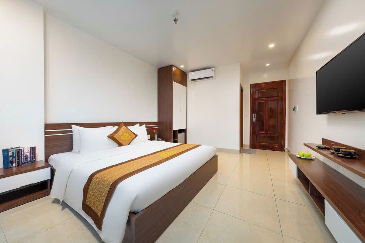 Una habitación de hotel con una cama grande, un televisor montado en la pared y una mesita de noche de madera.