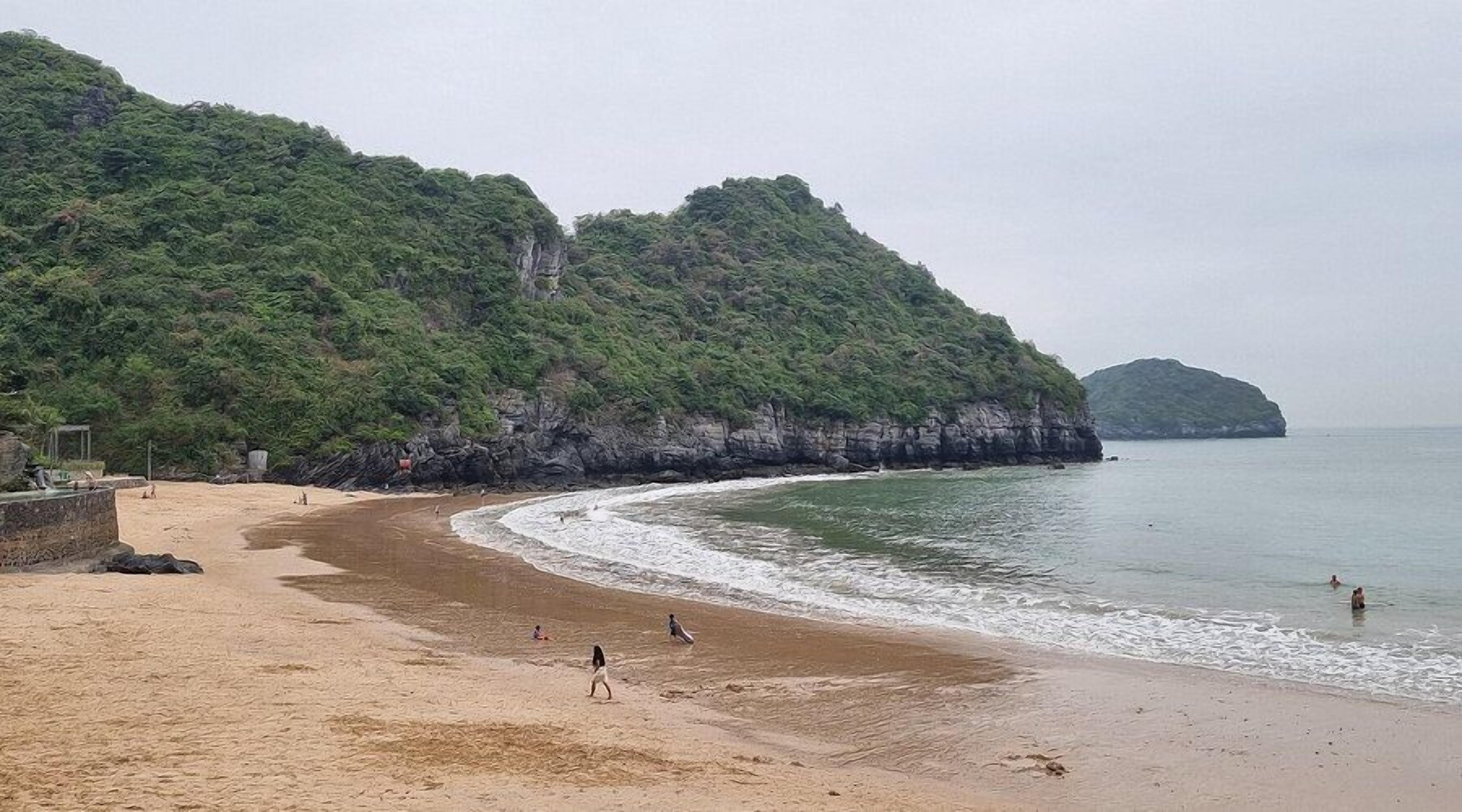 A beach with a sandy shore, a rocky cliff, and a calm sea.