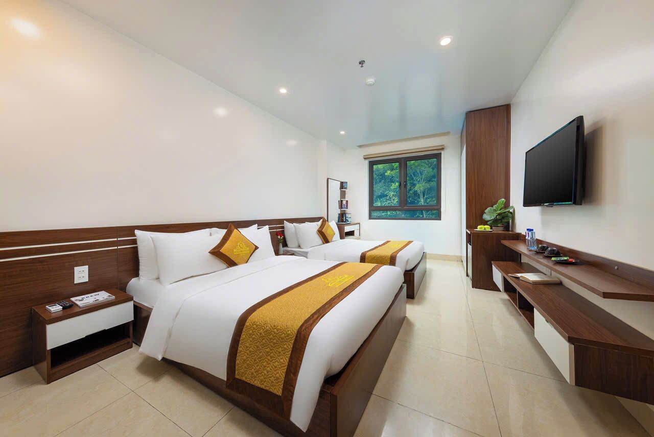 A hotel room with two beds, a TV, a desk, and a window with a view of trees.
