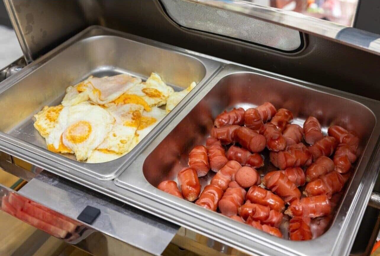 A buffet with two trays, one containing scrambled eggs and the other with sausages.