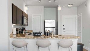 Cozinha moderna com ilha central, banquetas, eletrodomésticos de aço inoxidável e iluminação pendente.