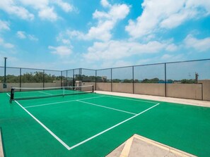 Ein Tennisplatz im Freien mit Netz, umgeben von einem Maschendrahtzaun, unter blauem Himmel.