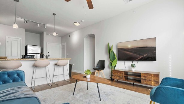 Uma sala de estar moderna com uma televisão grande, uma mesa de centro de madeira e sofás azuis.