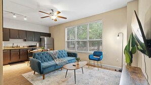 A modern living room with a blue sofa, a coffee table, and a TV mounted on the wall. - SOCO City Views  | Pool + Gym + Racquetball + Laundry + Pkg (Austin)