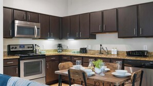 A modern kitchen with dark wood cabinets, stainless steel appliances, and a granite countertop. - SOCO City Views  | Pool + Gym + Racquetball + Laundry + Pkg (Austin)
