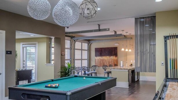 A pool table in a room with a modern design, including a bar area and a seating space with chairs. - SOCO City Views  | Pool + Gym + Racquetball + Laundry + Pkg (Austin)