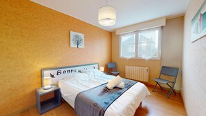 Ein Schlafzimmer mit einem Bett, Nachttischen, einem Sessel, einem Heizkörper und einem Fenster.
