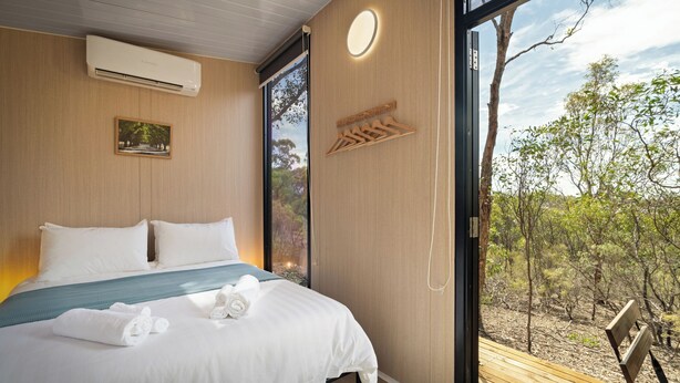 A modern bedroom with a large bed, a view of the outdoors, and a wooden bench. - Eucalypt Escape by Tiny Away (Coimadai)