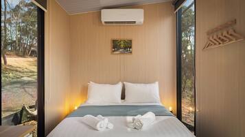 Een moderne slaapkamer met een groot bed, een vastgemaakt airco-apparaat, een ingelijst kunstwerk en houten kledinghangers aan de muur.