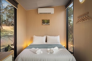 A modern bedroom with a large bed, a mounted air conditioner, a framed picture, and wooden hangers on the wall.