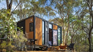 A modern cabin with a wooden exterior, large windows, and a fire pit area. - Eucalypt Escape by Tiny Away (Coimadai)