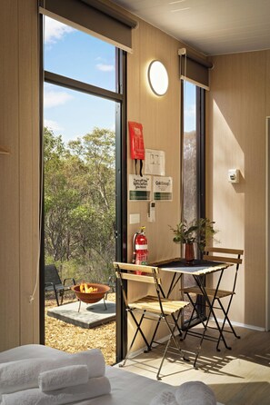 A modern room with large windows, a fire pit, and a view of trees. - Eucalypt Escape by Tiny Away (Coimadai)
