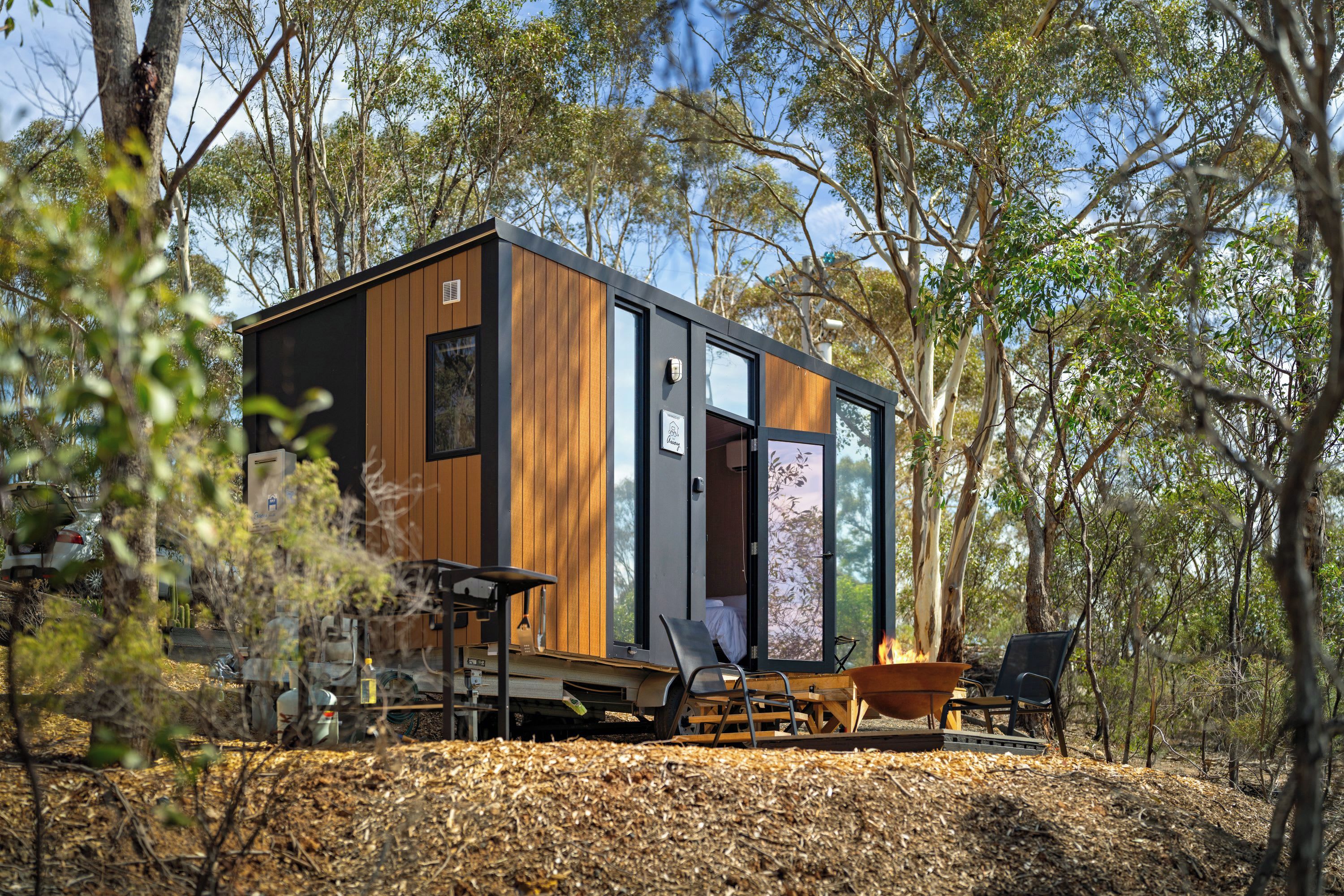 A modern cabin with a wooden exterior, large windows, and a fire pit area.