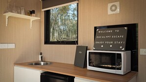 A compact kitchen with a sink, a microwave, and a window overlooking a forest. - Eucalypt Escape by Tiny Away (Coimadai)