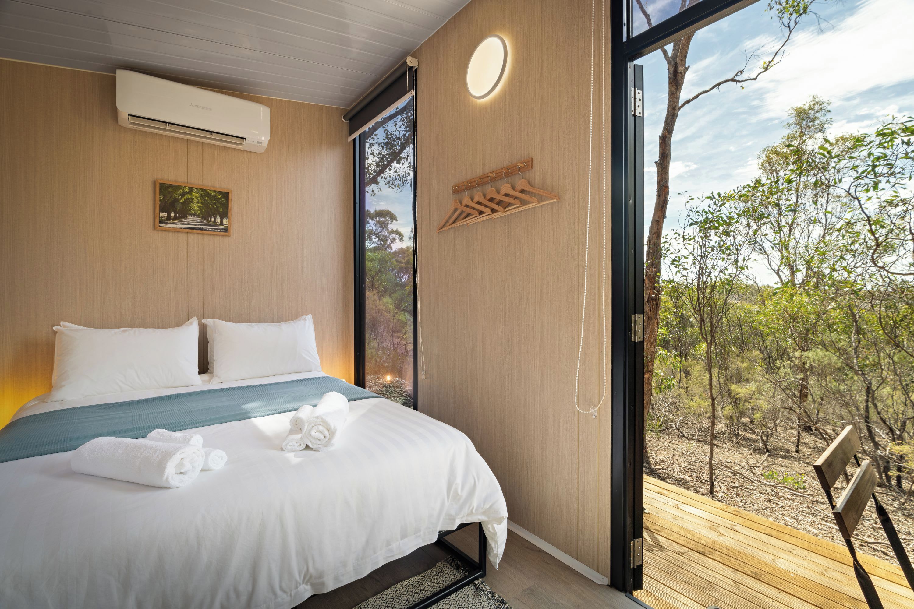 A modern bedroom with a large bed, a view of the outdoors, and a wooden bench.