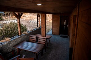 An outdoor wooden deck with benches and tables, stone walls, and a view of a landscaped area. - Villa in Jeseniky With Sauna & Mountain Views (Bela pod Pradedem)