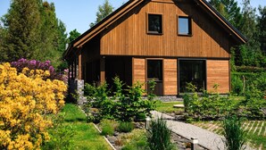 A modern wooden house with a sloped roof, large windows, and a well-maintained garden with various shrubs and flowers. - Villa in Jeseniky With Sauna & Mountain Views (Bela pod Pradedem)